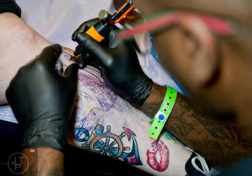 Anthony Locke (right) tattoos Gunda Blankenship's leg during the Atlanta Tattoo Expo at the Wyndham Atlanta Galleria hotel on Saturday, June 7, 2014. 