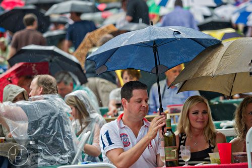 Jeff Johnson (left) and his wife Christy Brown Johnson try to protect themselves from the rain as they wait for Hall & Oates to come to the stage at Chastain Park Amphitheatre in Atlanta on Sunday, June 15, 2014.   