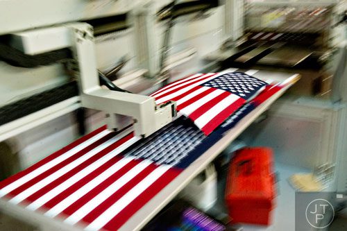 American flags are moved into piles by a machine after they are cut to the correct size at U.S. Flag Makers in Marietta on Wednesday, July 2, 2014.  