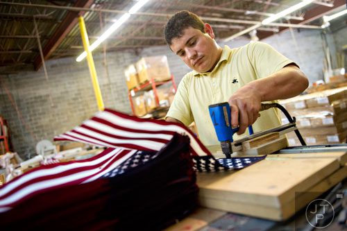 Rosendo Flores places an American flag into a pile at U.S. Flag Makers in Marietta on Wednesday, July 2, 2014.  