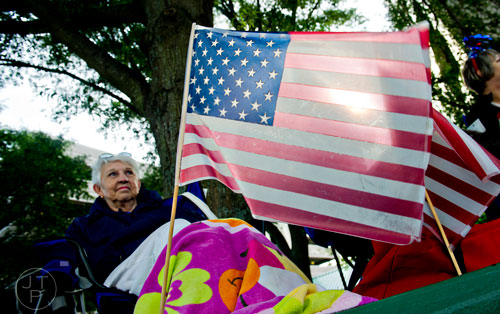 An American flag glows in the morning light as Jo Bagwell (left) waits for the start of the Marietta Freedom Parade on Friday, July 4, 2014. 