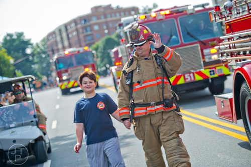 Marietta Fire Lt. Jeff Guest (right) holds his son Nathaniel's hand as they march down Roswell St. during the Marietta Freedom Parade on Friday, July 4, 2014. 