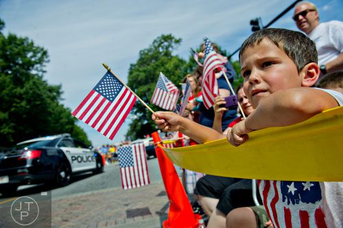 Austin Lenz (right) holds an American flag as he watches the Marietta Freedom Parade move towards Historic Marietta Square on Friday, July 4, 2014. 