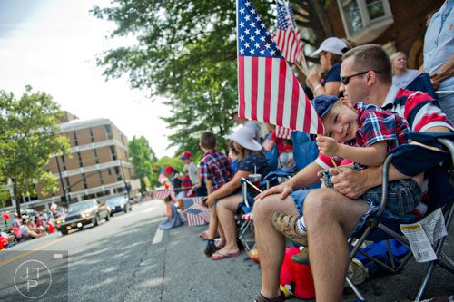 Corbin Eskridge (right) holds an American flag while sitting on his father Daniel's lap as they watch the Marietta Freedom Parade move towards Historic Marietta Square on Friday, July 4, 2014. 