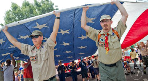 Scout Masters Dan Bird (left) and Matt McNeil hold up an American flag as they march through Historic Marietta Square during the city's  Freedom Parade on Friday, July 4, 2014. 