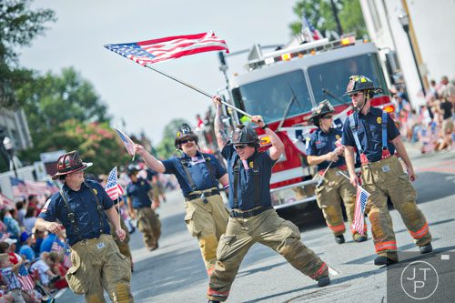 Cobb County firefighter Shane Turner (center) waves an American flag as he marches past Historic Marietta Square during the city's  Freedom Parade on Friday, July 4, 2014. 