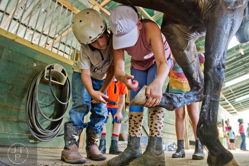 Bennett Lindseth (left) and Skylar Skalicky clean out a horse's shoes before going on a trail ride during horseback riding summer camp at the Ellenwood Equestrian Center in Ellenwood on Wednesday, July 9, 2014.  
