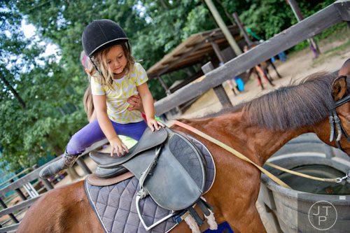 Avery Afeman climbs up on her horse during horseback riding summer camp at the Ellenwood Equestrian Center in Ellenwood on Wednesday, July 9, 2014.    