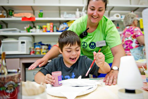 Marc Piccolo (left) paints a piece of pottery as counselor Heather Miller helps him during Camp Happy Hearts in Alpharetta on Tuesday, June 17, 2014. 