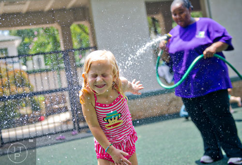 Quinn Stammel (left) cools off as LeTanya McKan sprays her with water during summer camp at the Frazer Center in Atlanta on Thursday, June 19, 2014. 