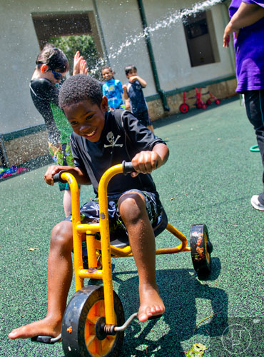 Elijah Williams pedals away from LeTanya McKan as she sprays campers with water during summer camp at the Frazer Center in Atlanta on Thursday, June 19, 2014. 