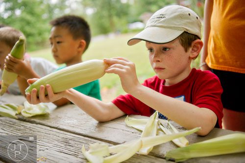 Jack Hughes (right) shucks an ear of corn as he and other campers make corn husk dolls during summer camp at Autrey Mill Nature Preserve in Johns Creek on Monday, July 14, 2014.