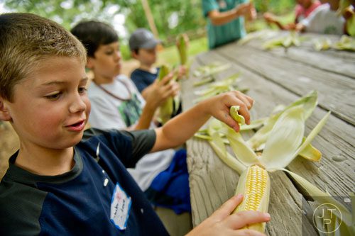 Tucker Lowe (left) shucks an ear of corn as he and other campers make corn husk dolls during summer camp at Autrey Mill Nature Preserve in Johns Creek on Monday, July 14, 2014.  