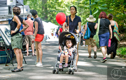 Shoko DeSutter (center) pushes her daughter Amelia in a stroller as they pass by artist booths during the Grant Park Summer Shade Festival in Atlanta on Saturday, August 23, 2014. 