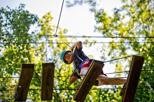Mackenzie Peace makes her way across a tree top bridge on the high ropes course at Camp Timber Ridge in Mableton on Thursday, July 17, 2014. 