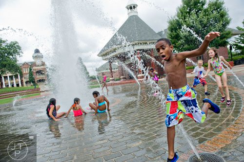 Makhi Melero (right) leaps through a stream of water as he and other children play in the fountain at the Duluth Town Green on Tuesday, July 22, 2014. 