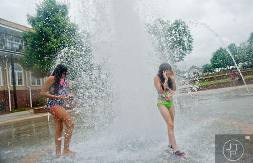 Addison Schulz (right) and Abigail Almaraz get wet as they walk through the fountain at the Duluth Town Green on Tuesday, July 22, 2014.  