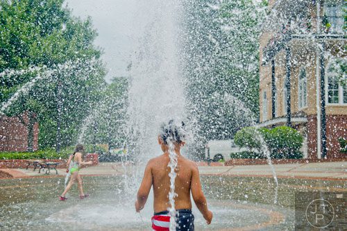 Anas Jarady (center) stands still to let a stream of water pound against the back of his head as he plays in the fountain at the Duluth Town Green on Tuesday, July 22, 2014. 