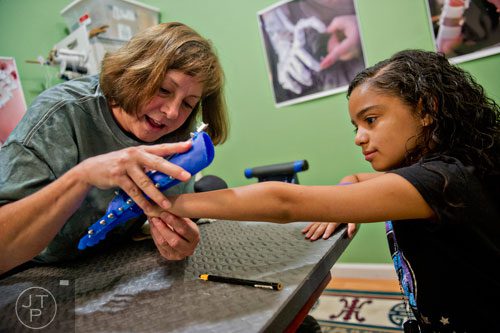 Ty Esham (left) helps fit 10-year-old Anastasia Rivas with her new robohand assistive device at her office in Decatur on Tuesday, August 5, 2014. 