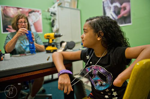 10-year-old Anastasia Rivas (right) watches Ty Esham make small adjustments to her new robohand assistive device at Esham's office in Decatur on Tuesday, August 5, 2014. 