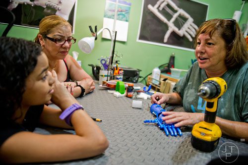 Ty Esham (right) goes over care instructions for a robohand assistive device with 10-year-old Anastasia Rivas (left) and her grandmother Wanda Oliveras as she makes small adjustments during a fitting session at her office in Decatur on Tuesday, August 5, 2014.