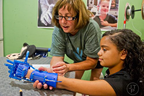 Ty Esham (center) helps 10-year-old Anastasia Rivas try out her new robohand assistive device in Esham's office in Decatur on Tuesday, August 5, 2014. 