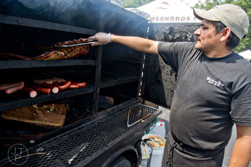 Carter Ramirez flips ribs and sausages in a smoker during the Decatur BBQ, Blues & Bluegrass Festival at Harmony Park in Decatur on Saturday, August 16, 2014.