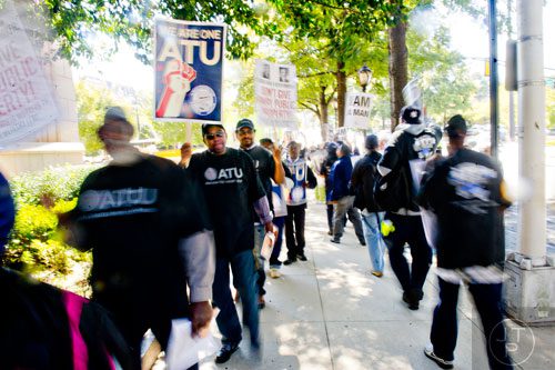 Curtis Jeffrey (left) and Monti Wilson walk the sidewalk carrying signs and chanting with around 150 other MARTA employees and retirees as they rally in front of the law offices of MARTA Board Chair Robbie Ashe off of W. Peachtree St. in Atlanta on Monday, October 6, 2014. 