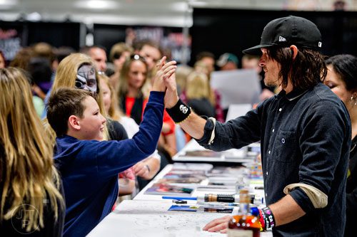 Norman Reedus (right), who portrays Daryl Dixon on the Walking Dead, gives a high five to Drew Tomlinson as he signs autographs during Walker Stalker Con in Atlanta on Sunday, October 19, 2014. 