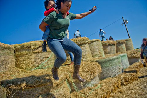 With her son Ricardo clinging to her back, Shanika Smith takes a leap off of the last layer of hay bales at Corn Dawgs in Loganville on Sunday, October 5, 2014.