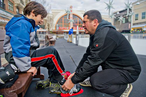 Julien Seher (left) gets help putting on his skates from his father Parseg before getting on the ice rink at Avalon in Alpharetta on Sunday, November 30, 2014. 