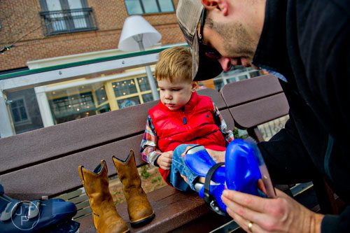 Wyatt Pope (left) gets help putting on his skates from his father David before getting on the ice rink at Avalon in Alpharetta on Sunday, November 30, 2014. 
