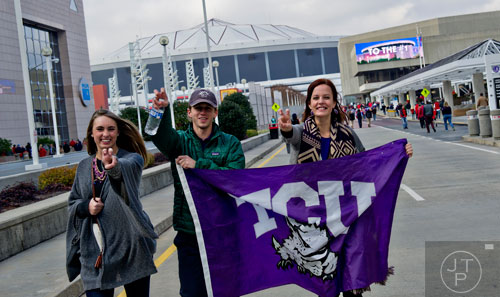 Emily Walden (left), Michael Walton and Hailee Pipes carry a TCU flag as thousands of people walk towards the Georgia Dome in Atlanta to watch the Chick-fil-A Peach Bowl on Wednesday, December 31, 2014. 