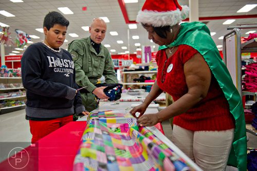 Marleen Tomlinson (right) helps wrap presents for Adonis Reyes (left) as Brookhaven Police Ofc. John Clifford places more gifts on the table during the first annual Brookhaven Police Shop with a Badge event at the Target off of North Druid Hills in Atlanta on Saturday, December 13, 2014.