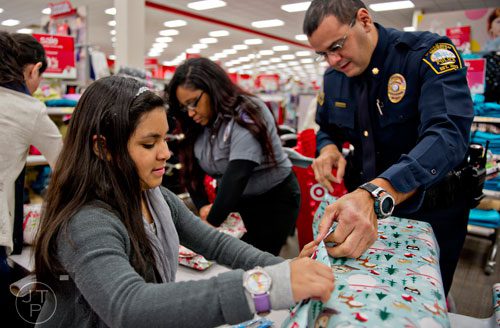 Denisse Rocha (left) helps Brookhaven Police Maj. Juan Grullon wrap a present she bought for her family during the first annual Brookhaven Police Shop with a Badge event at the Target off of North Druid Hills in Atlanta on Saturday, December 13, 2014. 