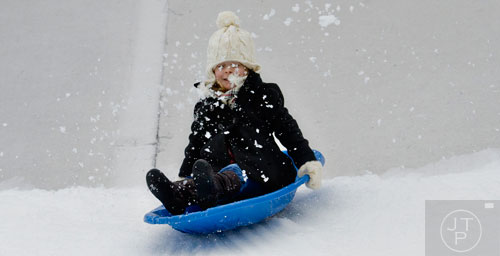 Snow kicks up in Reagan Isbell's face as she zooms down the hill in her sled during Snow Mountain at Stone Mountain Park on Sunday, December 21, 2014. 