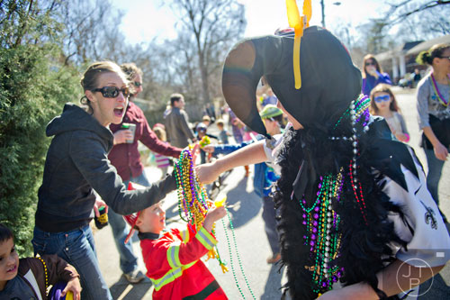 Eddie Galatas (right) hands a pile of beads to Courtney Goetzel and her son Miles as they watch the Mead St. Mardi Gras parade pass by on Saturday, February 7, 2015.