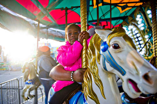 Niya Thomas holds onto her horse as she rides the Merry-Go-Round as the sun sets over downtown at the Atlanta Fair on Wednesday, March 4, 2015.