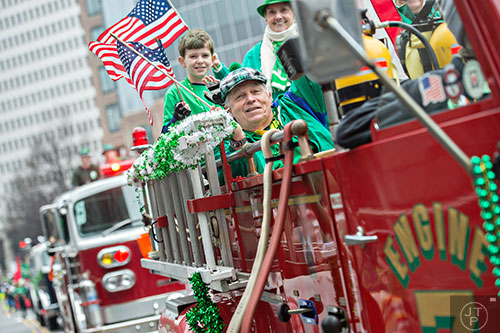 John Crispino (center) waves an American flag as he rides down Peachtree St. in a fire truck during the 2015 Atlanta St. Patrick's Parade on Saturday, March 14, 2015. 