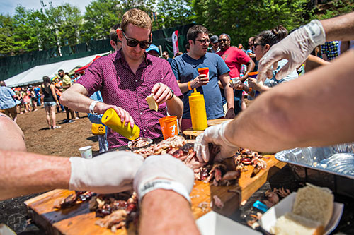 Robert Christopher (center) pours some sauce on his barbeque during the Hogs & Hops Festival at The Masquerade in Atlanta on Saturday, April 11, 2015.