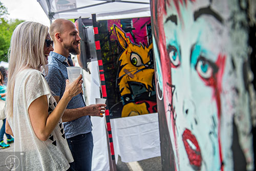 Kat Harding (left) and Marc Corbett check out Jeff Riggan's artwork during the Inman Park Festival in Atlanta on Saturday, April 25, 2015. 