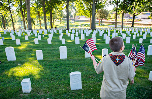 Nicholas Wolfson carries a handful of flags as he places them at the graves in the Marietta National Cemetery on Saturday, May 23, 2015. 