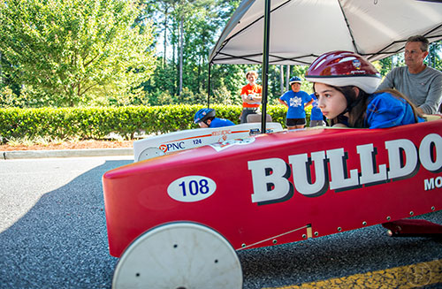 Alexys Grivakis (right) and Soma Hall take off from the starting line as Erik Christensen (center) lowers the gate during the All American Dunwoody Soap Box Derby at the First Baptist Church of Atlanta in Dunwoody on Saturday, June 6, 2015. 