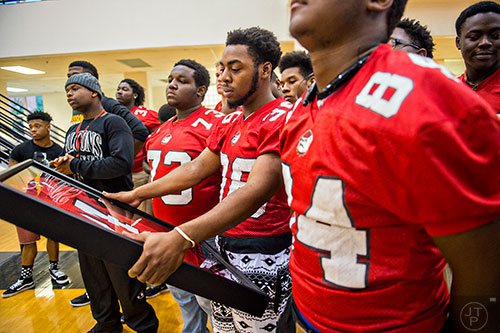 Shawn Odom (center) holds  Wali Clanton Jr.'s jersey in a shadow box before he and other members of the Dutchtown High School football team present the gift to Clanton's mother during the memorial service on Thursday, June 18, 2015. 