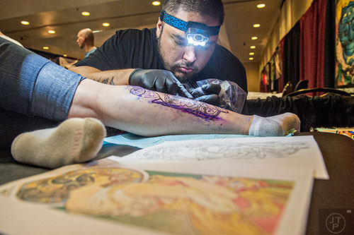 Matthew Gasca (right) works on a leg tattoo for Pacie Jordan during the 19th annual Atlanta Tattoo Expo at the Wyndham Atlanta Galleria hotel on Saturday, June 20, 2015. 