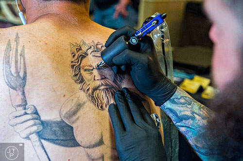 Deano Cook (hands) works on tattooing Daniel Edwards' back during the 19th annual Atlanta Tattoo Expo at the Wyndham Atlanta Galleria hotel on Saturday, June 20, 2015. 