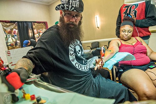Tatu Richie (center) turns to get more color on his machine as he works on Tierra Jenkins' tattoo during the 19th annual Atlanta Tattoo Expo at the Wyndham Atlanta Galleria hotel on Saturday, June 20, 2015. 