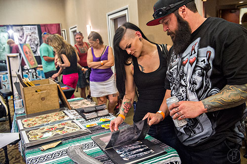 Jason Orsini (right) and Katie Morris look at Abdiel Pedraza's tattoo portfolio during the 19th annual Atlanta Tattoo Expo at the Wyndham Atlanta Galleria hotel on Saturday, June 20, 2015. 