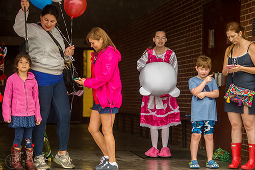 Kristen Hughes (center right) tries to find shelter from the pouring rain to keep her Hello Kitty costume dry before the start of the Avondale Estates 4th of July Parade on Saturday, July 4, 2015. 