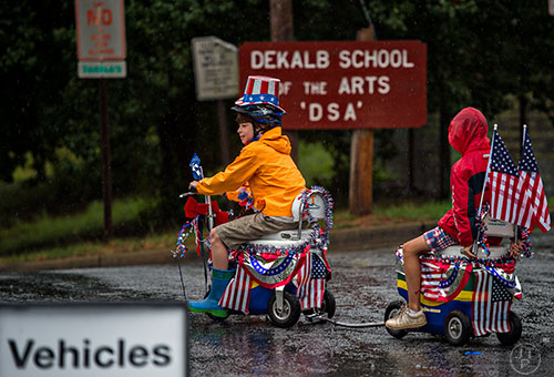 Dodge Hill (left) pulls Ben Kelly on a motorized cooler scooter in the pouring rain before the start of the Avondale Estates 4th of July Parade on Saturday, July 4, 2015. 